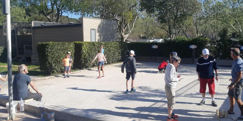 People of various ages playing an outdoor game on a gravel court, surrounded by cabins and trees at Parc Mogador
