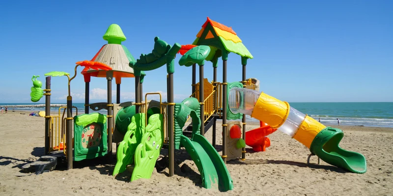 Colorful playground with slides and climbing structures on a sandy beach near the ocean at Italy Camping Village