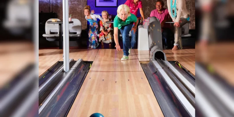A child rolls a bowling ball down the lane as family watches at Duinrell