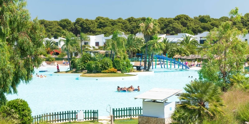 Group of people swimming in a large pool surrounded by greenery and buildings at I Turchesi Club Village