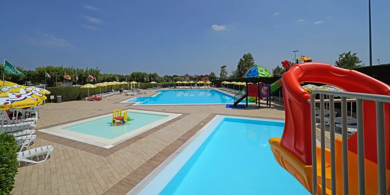 Three pools featuring slides and loungers surrounded by greenery and umbrellas under a clear blue sky at Tiglio
