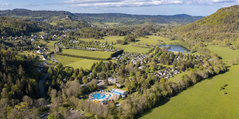 Aerial view of green countryside with campsites, pools, and scattered buildings amid forests and hills at La Ribeyre