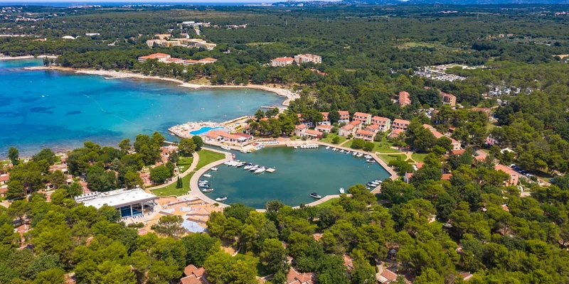 Aerial view of a coastal resort with villas, pine trees, and a marina with boats at Stella Plava Laguna