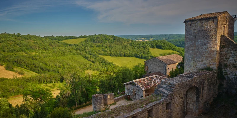 Stone fortress overlooks lush, hilly countryside under blue sky at Le Chêne Vert