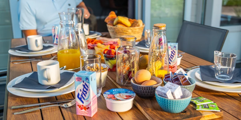 Breakfast table filled with juice, eggs, pastries, and yogurt, with a person seated at Europarcs Parc du Soleil