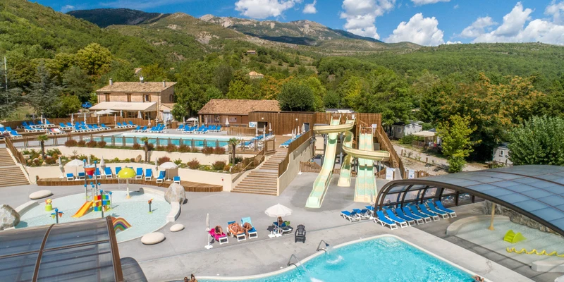 Swimming pools and water slides with people enjoying in a landscaped, mountainous rural resort setting at Terra Verdon 