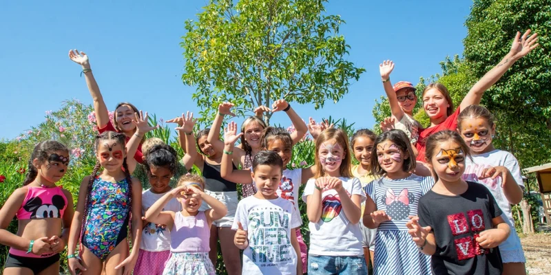 Children with face paint cheerfully pose together in a sunny outdoor garden at La Prairie 