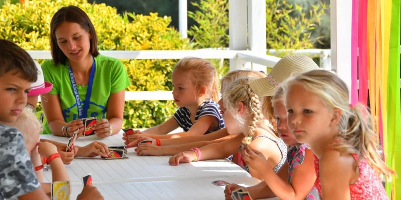 A group of children and a woman play a card game at a shaded outdoor table at Spiaggia e Mare