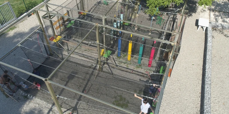 People navigating ropes and obstacles inside an elevated metal cage structure at Les Fontaines