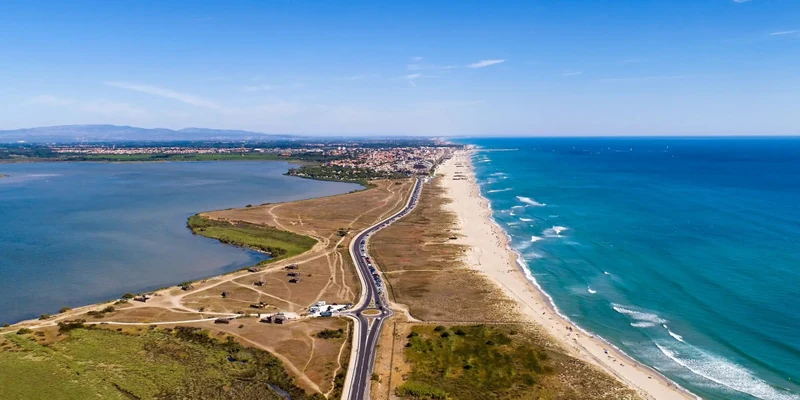 Overhead view: a road divides a beach and a lagoon, leading to a coastal town in the distance at Les Flamants Roses
