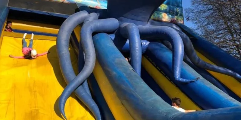 Children slide down an inflatable octopus-themed slide outdoors, surrounded by trees and blue sky at La Sirenetta