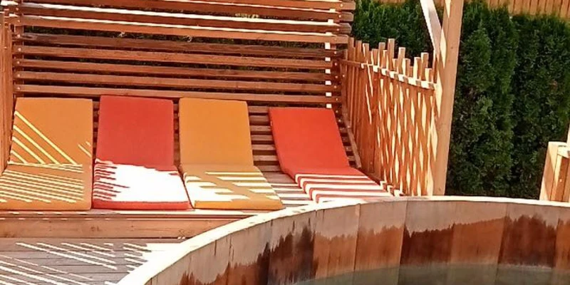 Wooden hot tub cooling under a slatted pergola near colorful lounge chairs at Clos du Pin