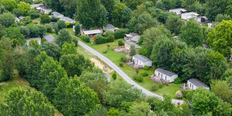 Cabins arranged along a road, surrounded by dense green trees and open grass at Marvilla Parks Le Domaine de la Brèche