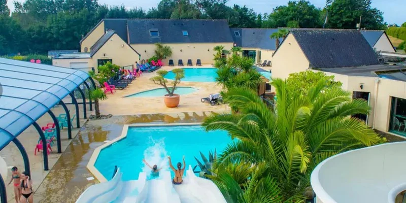 People sliding down water slides into a pool, surrounded by palm trees and buildings at Marvilla Parks Pommeraie de l'Océan