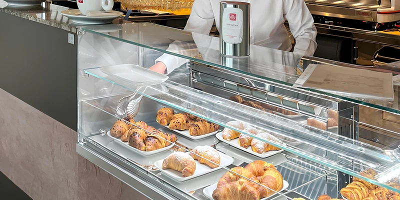 Pastries displayed in a glass case, served by a person in a café setting at Camping Mare Pineta