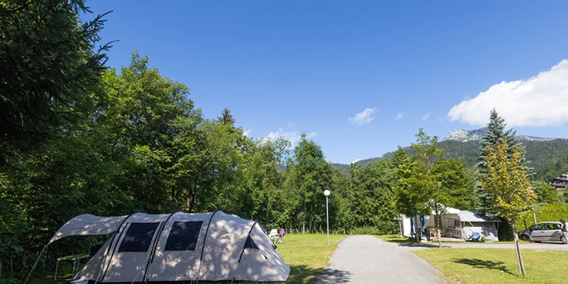 Tent standing on grassy area next to a paved path, surrounded by trees and mountains at Clos du Pin