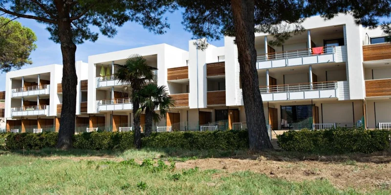 Modern apartment complex with balconies, situated among trees and surrounded by grass at Residence Carré Marine