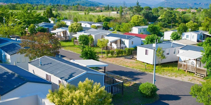 Rows of mobile homes sit among green trees and pathways under a cloudy sky at La Prairie 