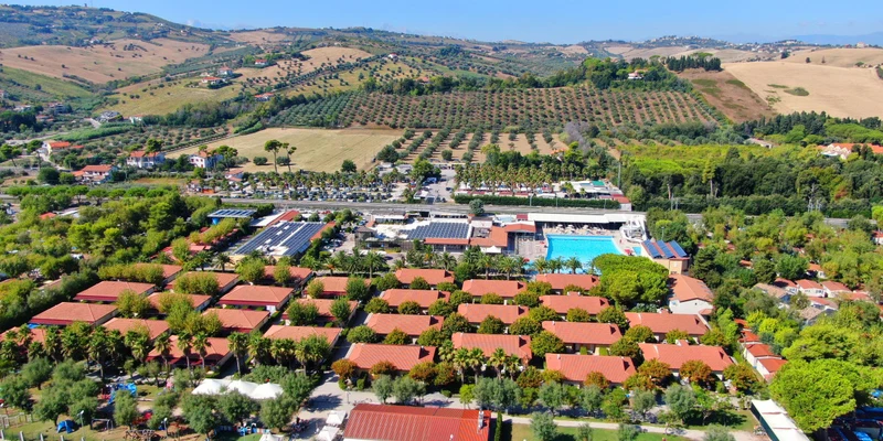 Aerial view of a campsite with red-roofed cabins, surrounded by lush hills and farmland at Villaggio Turistico Lido D Abruzzo