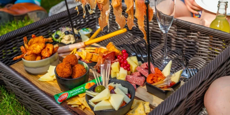Charcuterie board with meats, cheeses, and snacks arranged in a wicker basket outdoors at Europarcs Hoge Kempen