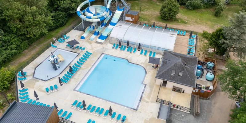 A swimming pool with slides and sunbeds, surrounded by trees and a building at Marvilla Parks Le Domaine de la Brèche