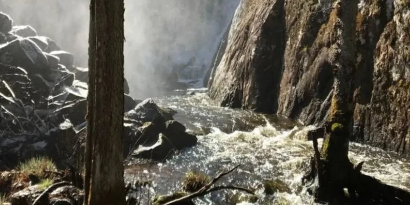 Waterfall cascading over rocky cliffs, surrounded by trees and mist, with a river flowing at Smaland Miniglamping