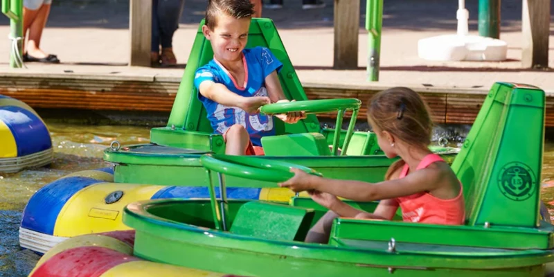 Children steering green bumper boats on water, enjoying a sunny day at an amusement park attraction at Duinrell