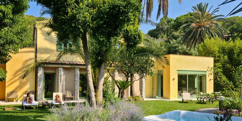 House surrounded by lush garden; two people relaxing on lounge chairs, trees and hot tub nearby at Rosselba le Palme
