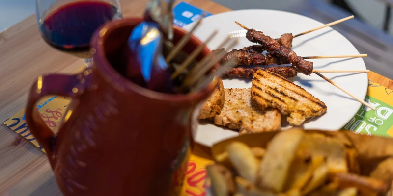 Plate of skewered meat and grilled bread, next to a pitcher and fries, on a wooden table at Stork Family Camping Village