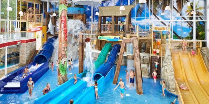 Children slide down colorful water slides, splashing into a pool inside a tropical-themed indoor water park at Duinrell