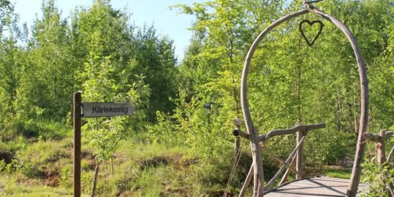 Wooden bridge with heart-shaped archway leads into lush green forest at Smaland Miniglamping