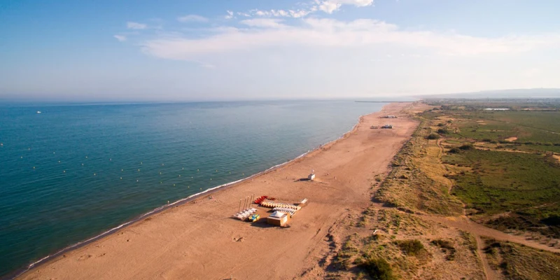 Aerial view of a sandy beach with scattered structures and people, beside a wide ocean and green landscape at Les Vagues