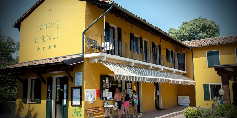 Bright yellow building with awning; people gathering at entrance; surrounded by potted plants at La Rocca Manerba