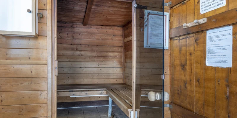 Wooden sauna with glass door and bench, situated indoors, surrounded by wooden paneling at Paradis Les Jonquilles