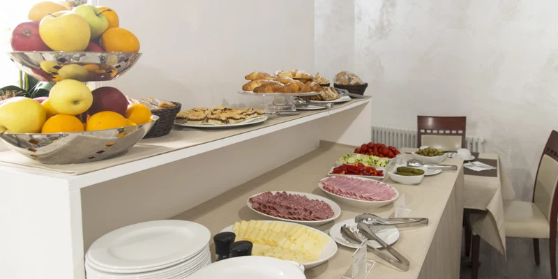 Breakfast buffet featuring fruit, pastries, cold cuts, cheese, and vegetables on a table in a small dining room at Residence Monica