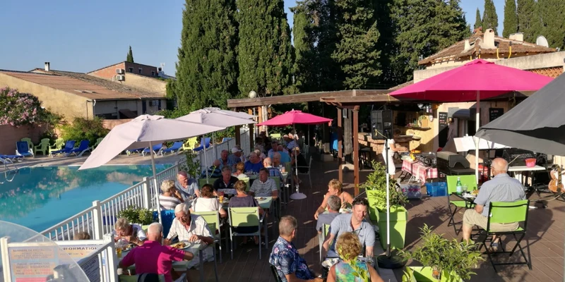 People dining on a patio beside a pool with umbrellas and trees in the background at Les Lauriers Roses