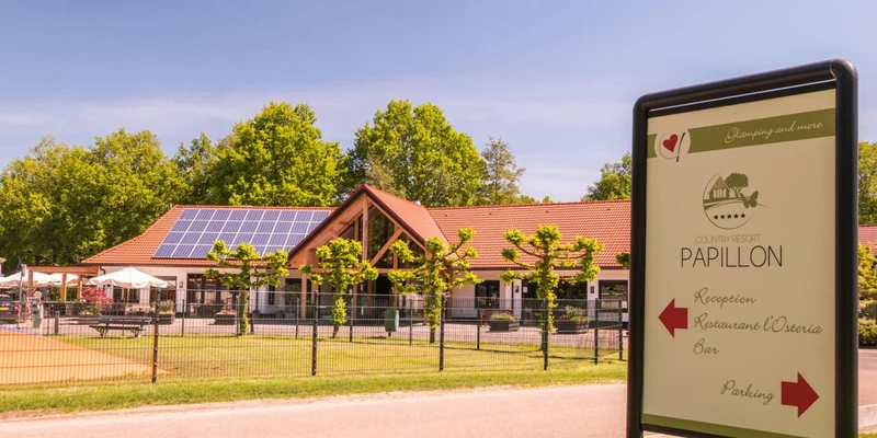 Sign indicates reception area near a large building with solar panels, surrounded by manicured trees and grass at Papillon Country Resort