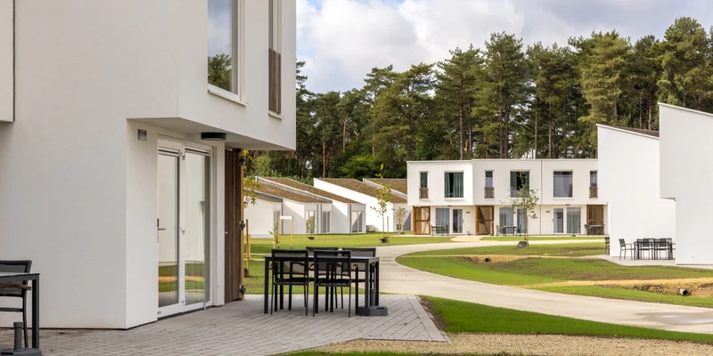 Tables with chairs outside modern white villas surrounded by grass and trees at Park Eksel