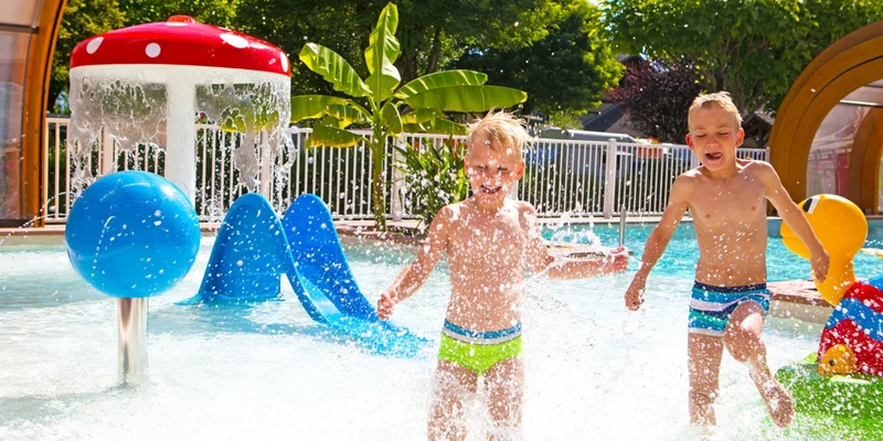 Two boys are playing and splashing in a kids’ pool with water features; bright, sunny day at Le Coin Tranquille