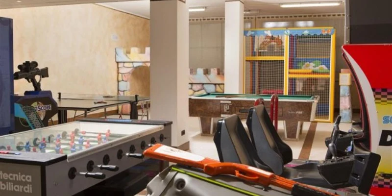 Arcade games display amidst foosball, racing simulators, and air hockey in an indoor recreation room at Poiano
