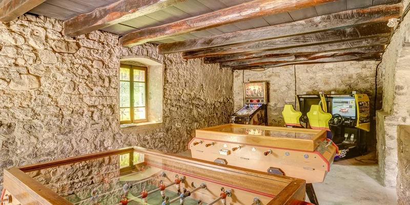 Foosball table in playroom with arcade games, wooden beams, and stone walls at La Ferme de la Serraz