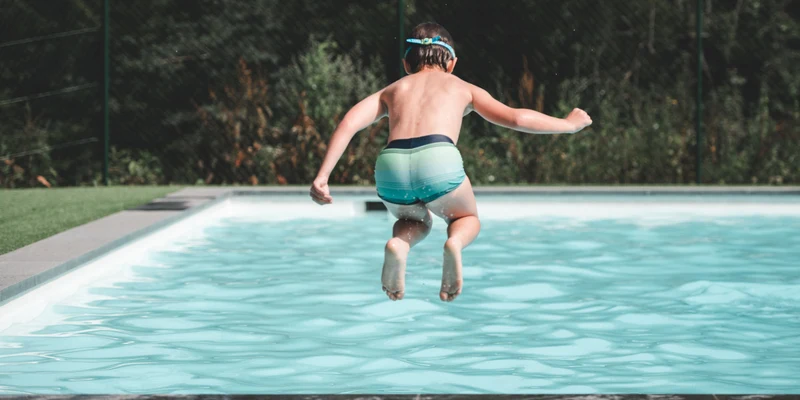 A child jumps into a swimming pool, surrounded by greenery and a fence at Verblijfpark Ardinam