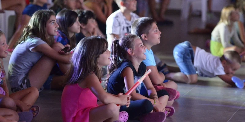 Children sitting on the floor, watching a performance, indoors at Camping Village Florenz