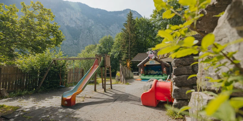 Playground slide stands in a mountain-surrounded area with greenery, inflatable playhouse visible in the background at Jungfrau