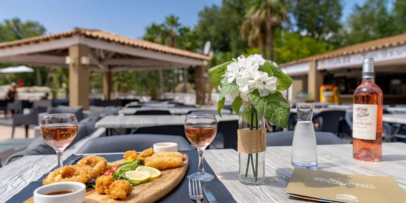 Platter with fried food and sauce on outdoor table, accompanied by rose wine and flowers at Les Vagues