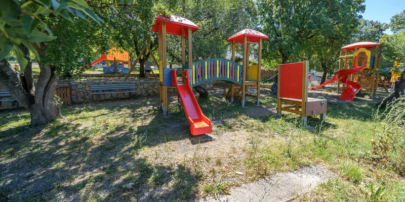 Colorful playground equipment under trees in a grassy area at Klenovica