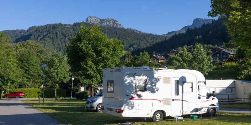 Camper van is parked on grass next to trees and mountains in the background at Clos du Pin
