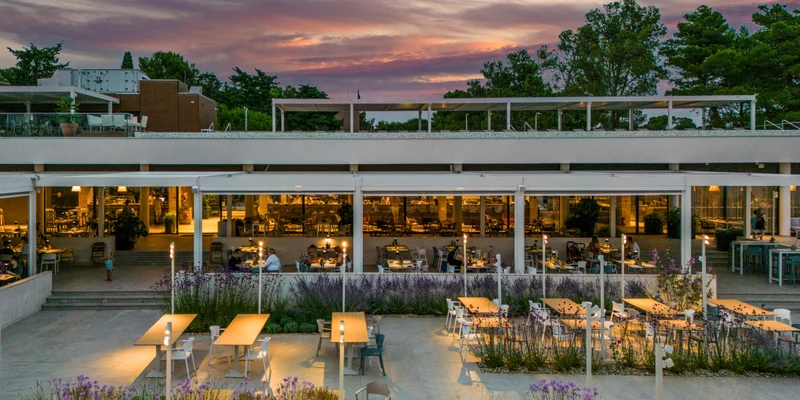 Restaurant terrace with tables and chairs, illuminated under a colorful sunset, surrounded by trees at Zaton Holiday Resort