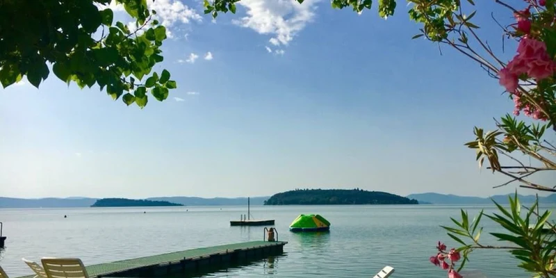Lounge chairs overlook a calm lake with a wooden dock, inflatable platform, and distant islands, surrounded by foliage at Punta Navaccia