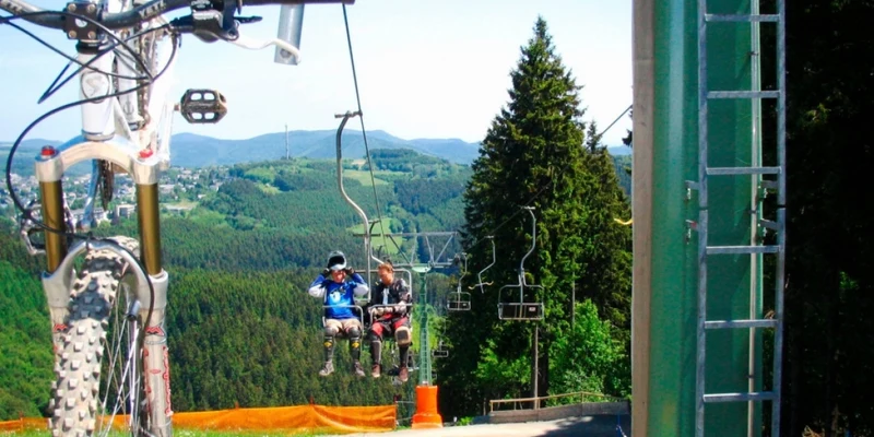Bicycles hang from a ski lift carrying people over a lush, mountainous landscape at Landal Winterberg